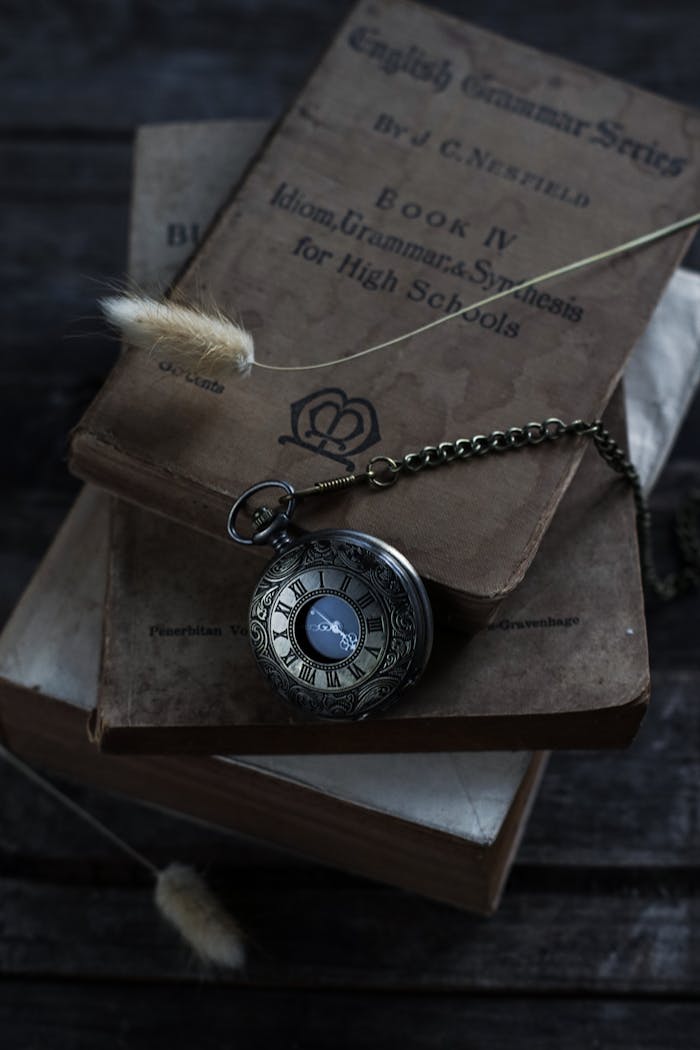 A stack of vintage books topped with an antique pocket watch and dry flowers, creating a nostalgic scene.