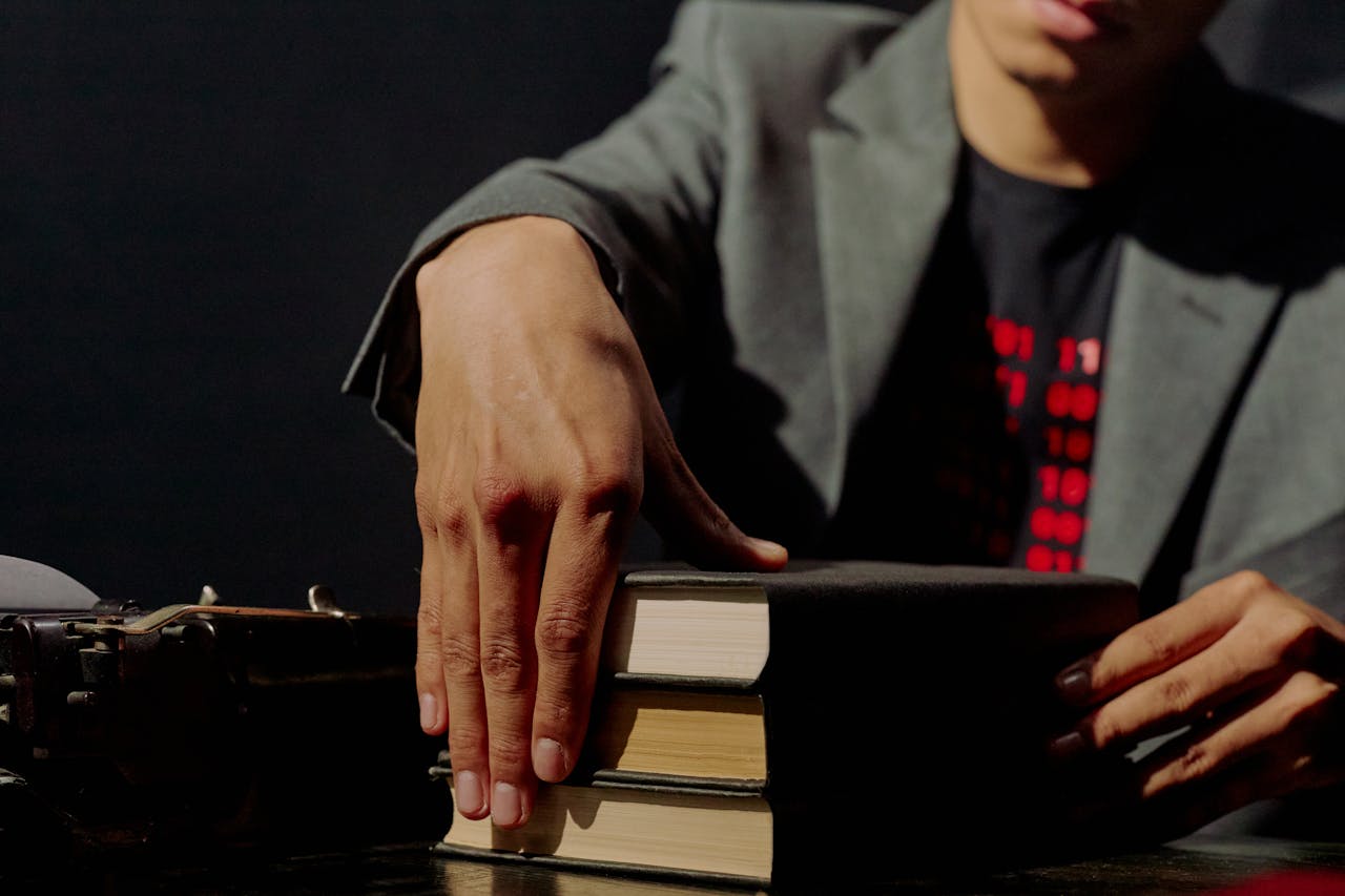 Close-up of a man in a suit placing books on a table with a typewriter nearby in a low-light environment.